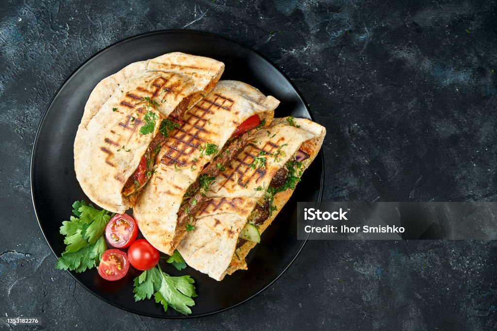 Three pita bread with vegetables, chicken and beef in a black plate on a dark background Pita Bread Stock Photo