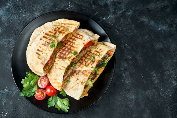 Three pita bread with vegetables, chicken and beef in a black plate on a dark background Three pita bread with vegetables, chicken and beef in a black plate on a dark background flatbread photos stock pictures, royalty-free photos & images
