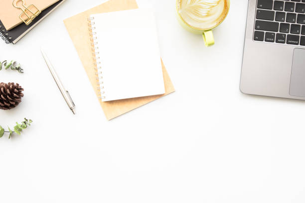 istock Small blank notebook with pen are on top of white office desk table with laptop computer and supplies. Top view with copy space, flat lay. 1353188344