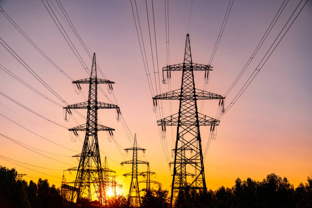 istock Multiple high-voltage towers silhouettes at sundown. Power lines at beautiful pink sunset light. Electricity power pylons in the last rays of setting sun. 1353189242