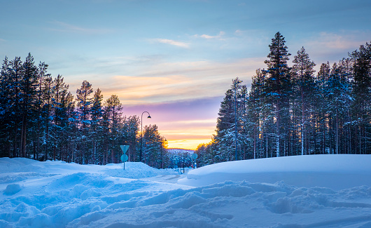 View of street with pine trees forest and mountain at sunset time with layer of colourful sky. At Kittila, Finland.