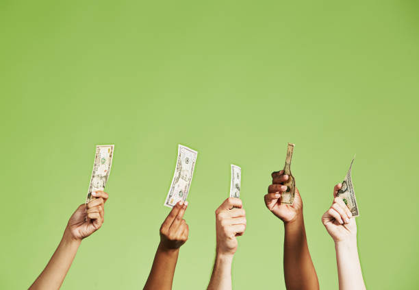 group of several diverse hands holding up us dollar banknotes of different denominations - hand raised arms raised multi ethnic group human hand imagens e fotografias de stock