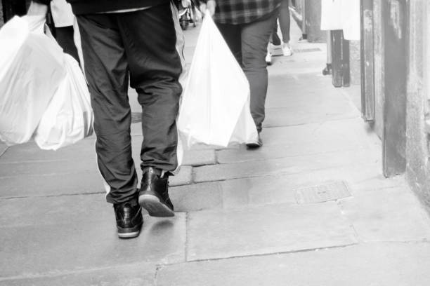 Santiago de Compostela, Spain- April 8, 2021: Rear black and white view of young man holding plastic shopping bags, walking down a pedestrian street.