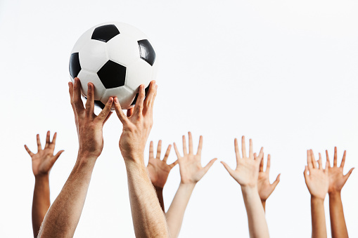 Group of people's hands waving, with soccer ball held aloft.