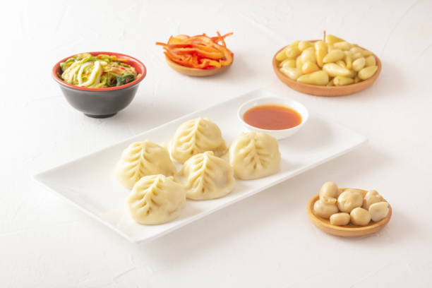istock Boiled dumplings, manti or wontons with minced meat in a plate with sauce on a white table along with pickled mushrooms, hot peppers and cabbage salad. 1353194792