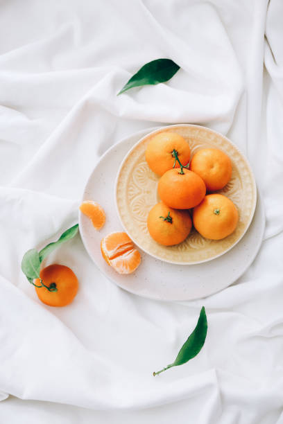 istock Fresh clementines with leaves on white fabric, top view 1353196231