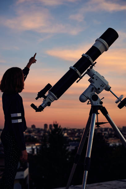 istock Girl with astronomical telescope stargazing under twilight sky. 1353197053