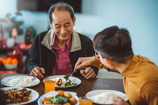 An Asian man sharing food to his father while enjoying reunion dinner at home during  Chinese New Year.