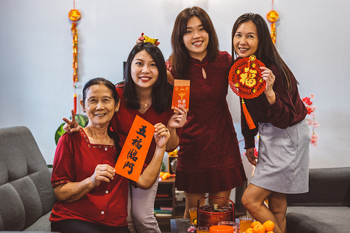 Three generations of joyful Asian family celebrating Chinese New Year and showing couplets with best wishes for upcoming year inscription at living room.
