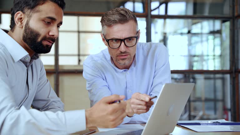 Two diverse business men discussing market data using laptop and digital tablet.