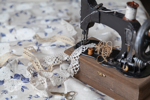 Vintage manual sewing machine and a skein of thread on a white fabric background with a blue pattern close-up. Braid and scissors lie nearby
