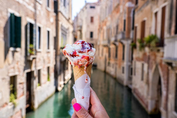 close up of hand holding strawberry gelato ice cream cone in front of canal - gelato imagens e fotografias de stock