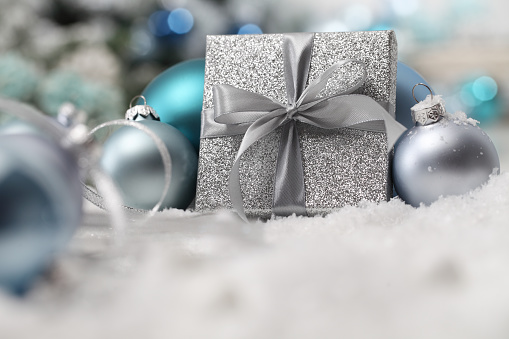 merry christmas background, silver gift present box with bow and ribbon, next to blue Christmas balls and snowflakes, useful as a greeting card template with copy space