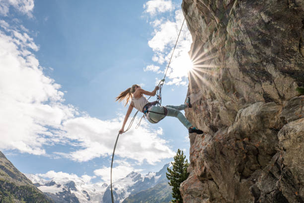 Mountain climber rappelling on rock face She looks down on the cliff. Mountains and glacier in distance rock face stock pictures, royalty-free photos & images