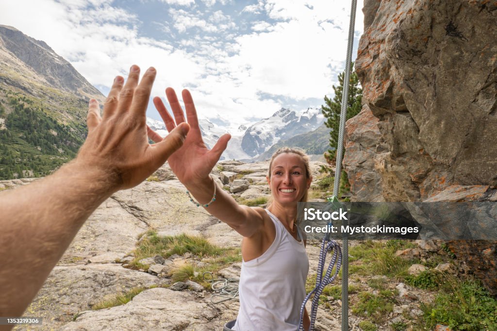 Mountain climber high fives with partner at the top of the rock POV from first person's perspective giving a high five. Mountains and glacier in distance Point of View Stock Photo