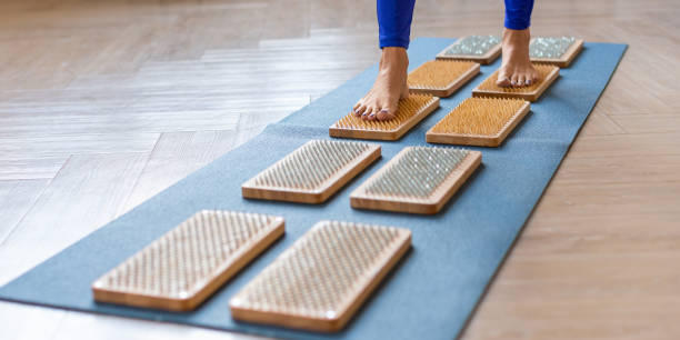 Female feet walking on a board with sharp nails over white background. Sadhu's board - practice yoga. Pain, trials, health, relaxation, cognition. Format photo 2x1