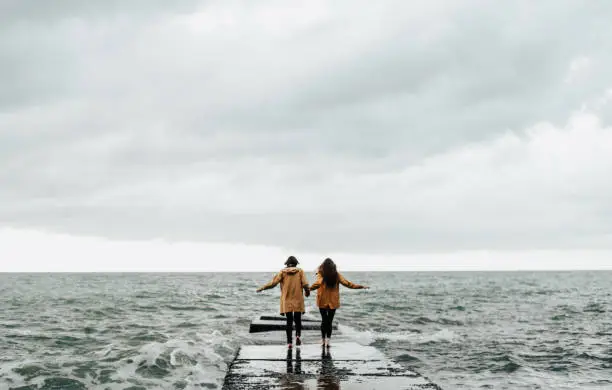 Photo of Man and  woman in yellow raincoats on the seashore.