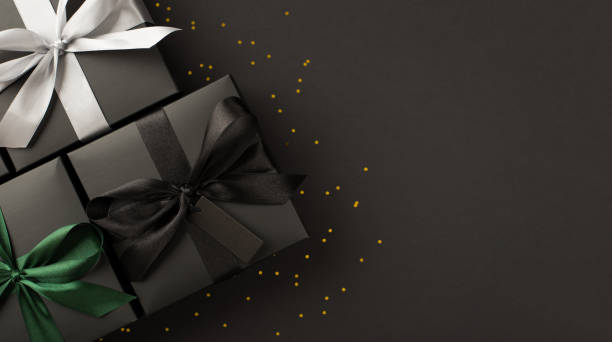 top view photo of three black gift boxes with black white and green ribbon bows and golden sequins on isolated black background with copyspace - green friday stockfoto's en -beelden