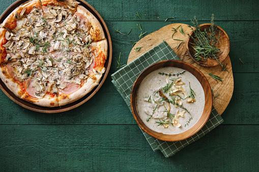 Creamy vegan wild mushroom soup with herb and vegetable chips (dairy free, gluten free). Pizza with mushroom. Flat lay top-down composition on wooden background.