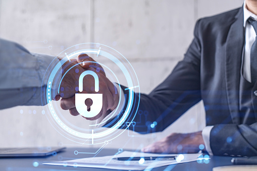 Handshake of two businessmen who enters into the contract to protect cyber security of international company. Padlock Hologram icons over the table with documents.