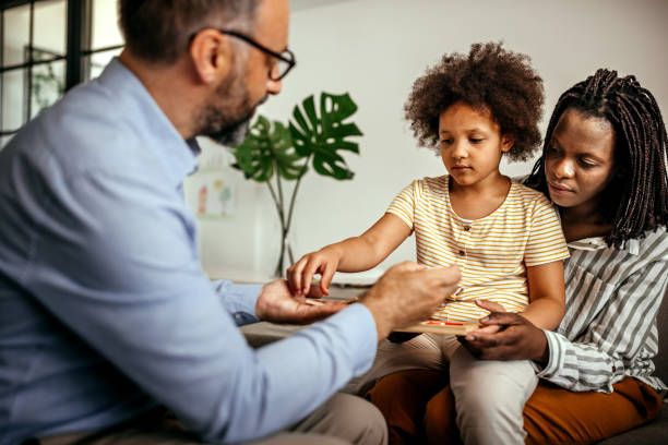 Mother having a therapy session for her daughter with male psychologist Little girl choosing toy with male psychologist mental health professional stock pictures, royalty-free photos & images