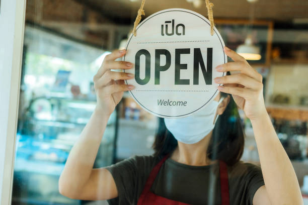 Lift lockdown. female staff wearing protection face mask turning Open sign board with Thai language on glass door in cafe coffee shop, cafe restaurant, small business owner, food and drink concept levantar el confinamiento. personal femenino con máscara facial de protección que gira tablero de letreros abierto con idioma tailandés en la puerta de vidrio en cafetería, cafetería restaurante, propietario de una pequeña empresa, concepto de comida