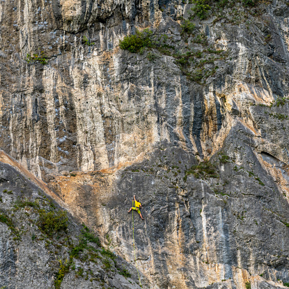 Esines, Italy - 12 October, 2021: rock climber dressed in bright yellow climbing a steep vertical difficult climbing route in the Italian Alps of Lombardy