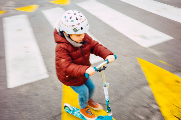 istock Young kid crossing the road with his scooter 1353232713