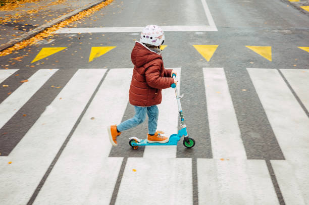 istock Young kid crossing the road with his scooter 1353232817