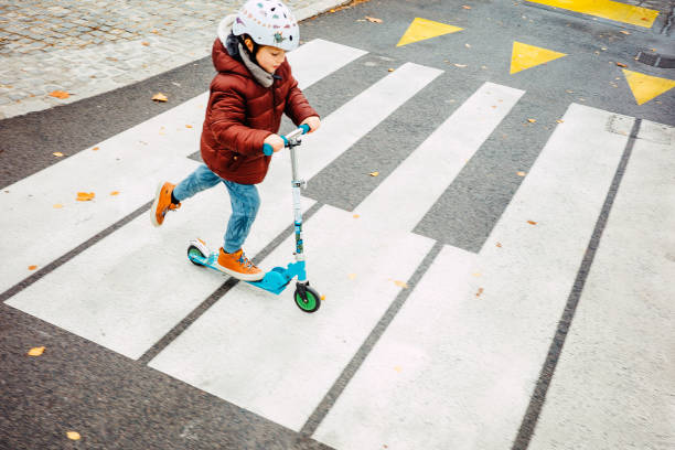 istock Young kid crossing the road with his scooter 1353232825