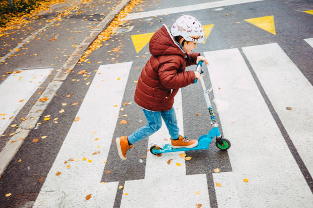 istock Young kid crossing the road with his scooter 1353232826
