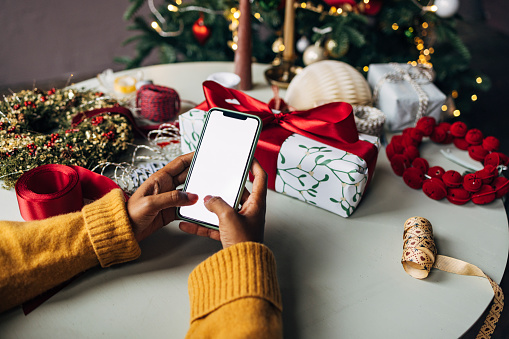 Hands of a Latin American woman using her smartphone to purchase Christmas gifts for her loved ones