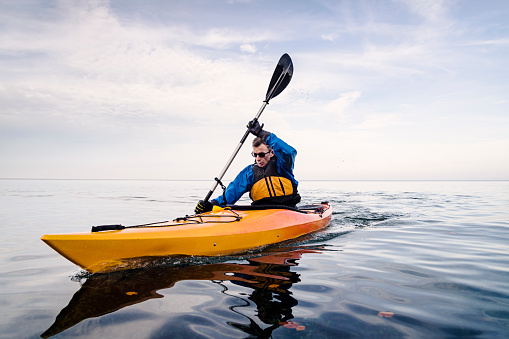 Portrait of a male sea kayaker in the water rowing his kayak around the island of Moen in the Baltic Sea in Denmark. Colour, horizontal format with some copy space.