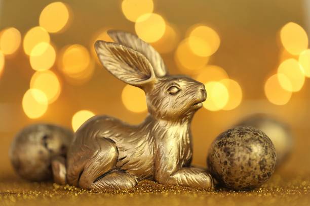 Easter bunny. Golden easter metallic bunny on golden glitter background with yellow bokeh.Religious holiday background. Easter holiday background in gold tones