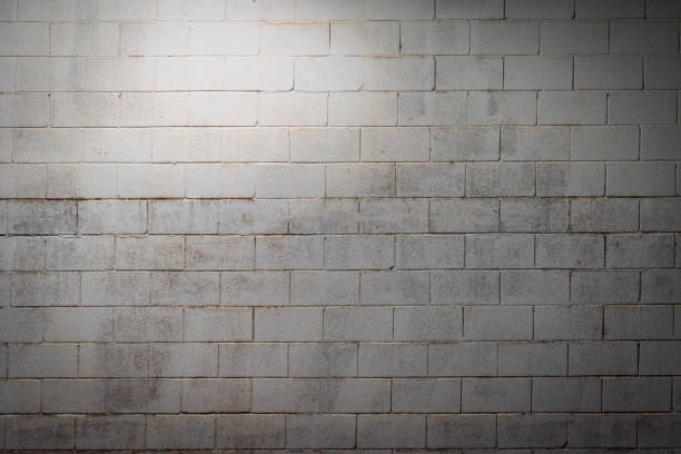 istock White block wall aged by humidity and illuminated with overhead light. Background. 1353240147