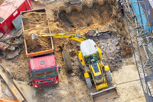 Excavator digs a hole and loads soil into the back of a truck, aerial top view