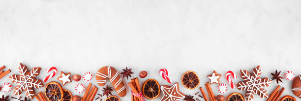 istock Christmas baking bottom border with cookies, peppermints and spices over a white marble background 1353245641