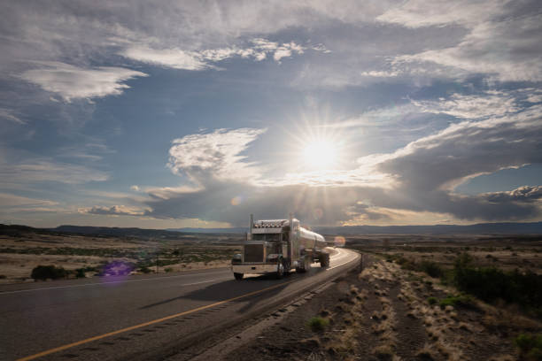 Brown Tanker Semi-Truck Speeding Down a Highway in the Utah Desert at Dusk under a dramatic sky stock photo