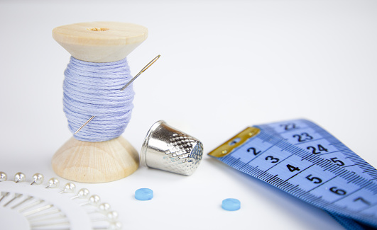 Sewing kit showing scissors, white buttons, tape measure, white thread, needle and thimble on black background.