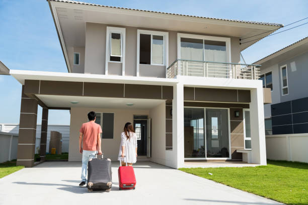 Asian Couple walk to their house and pull luggage. Moving to new home to start married life. Housing mortgage loan and refinance real estate or property.