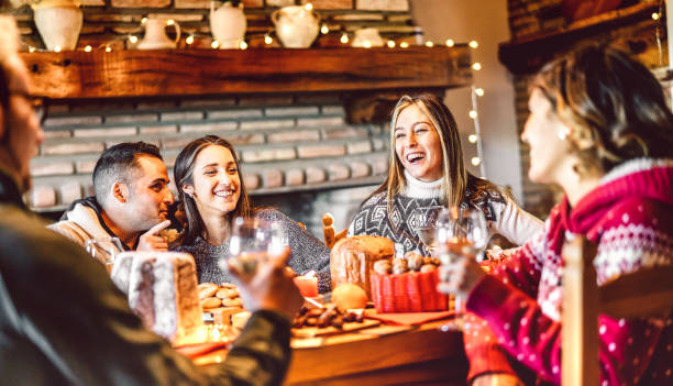 millenial people tasting christmas sweets at home supper party - new year's eve and winter holiday concept with young friends having fun eating together at evening - bulb string lights warm filter - celebrating friends winter imagens e fotografias de stock
