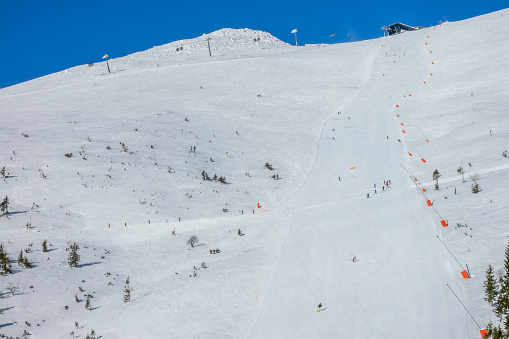 Slovakia. Winter ski resort Jasna. Sunny weather on a wide ski slope. Ski lift, several skiers and snow generators
