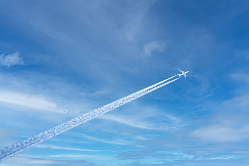 A large airliner flies in the air. There are white clouds and a trail behind the plane in the blue sky.