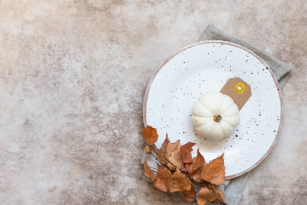 istock Festive autumn table place setting. Decorative white pumpkin, autumn leaves, craft ceramic plate and cutlery on concrete background. Fall composition. Flat lay, top view. 1353257491