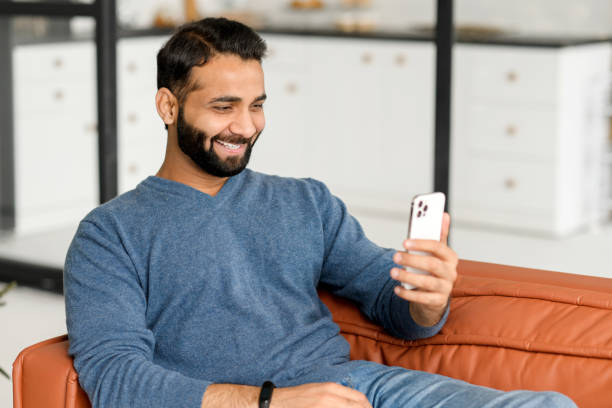 istock Hilarious Indian man in casual wear using smartphone for virtual meeting 1353257589