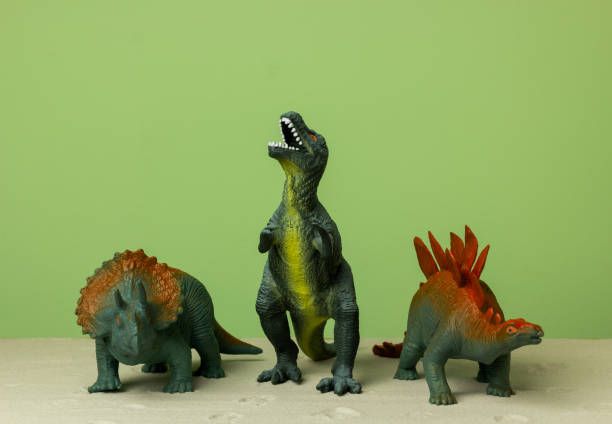 istock Toy dinosaurs stand on the sand on a green background. 1353257650
