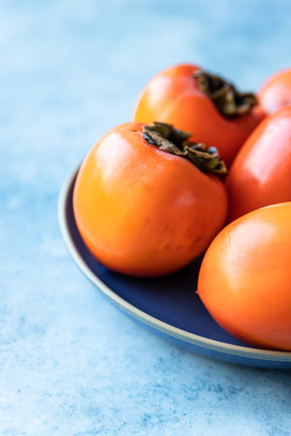 istock Fresh organic ripe persimmons on blue concrete background. 1353257789
