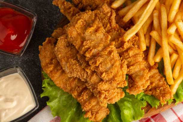 istock Breaded chicken strips with two kinds of sauces and fried potatoes on a stone background. Fast food on black stone background. Flat lay. Closeup 1353257837