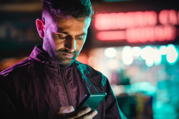 junger mann benutzt nachts auf der straße der stadt ein smartphone. - gelatinefilter stock-fotos und bilder