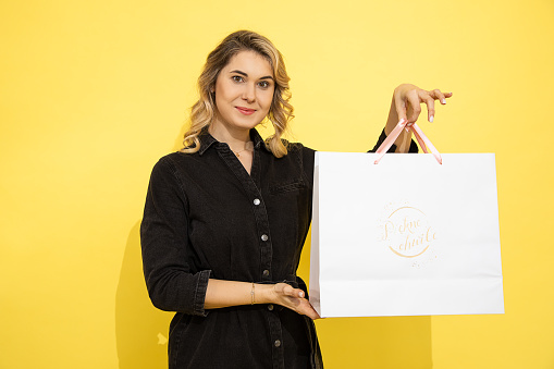 lovely young woman in casual clothing, happy with gift bags, shopping, spring holiday, yellow background, studio shot. Celebrating Woman's Day, birthday, Valentine's, anniversary. Copy space, blank.